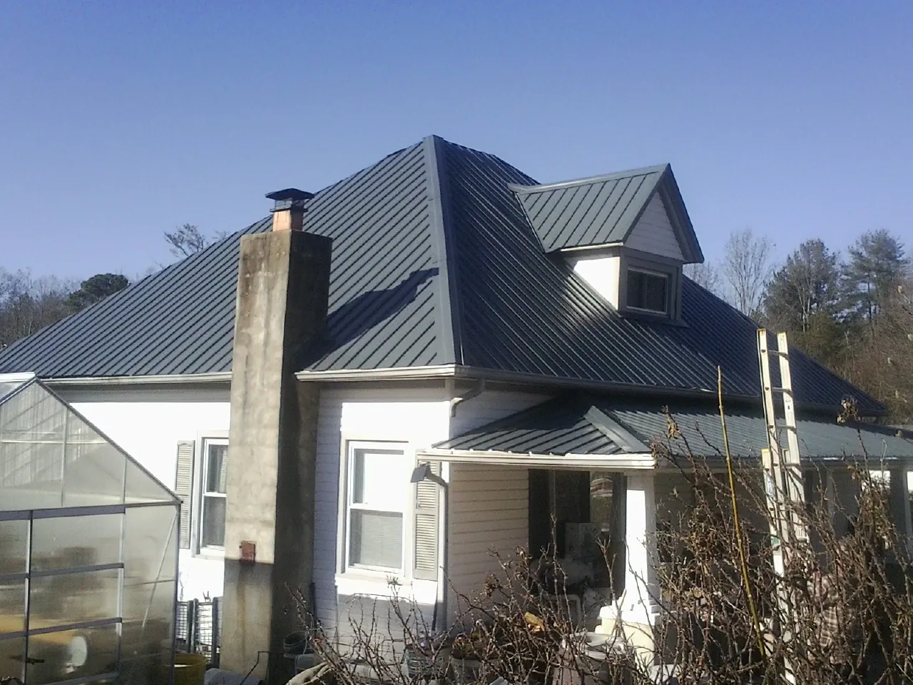 Dark blue standing seam metal roof on a white farmhouse with dormer — Slate & Tile Roof Repair by Roofing Brothers in Sprague