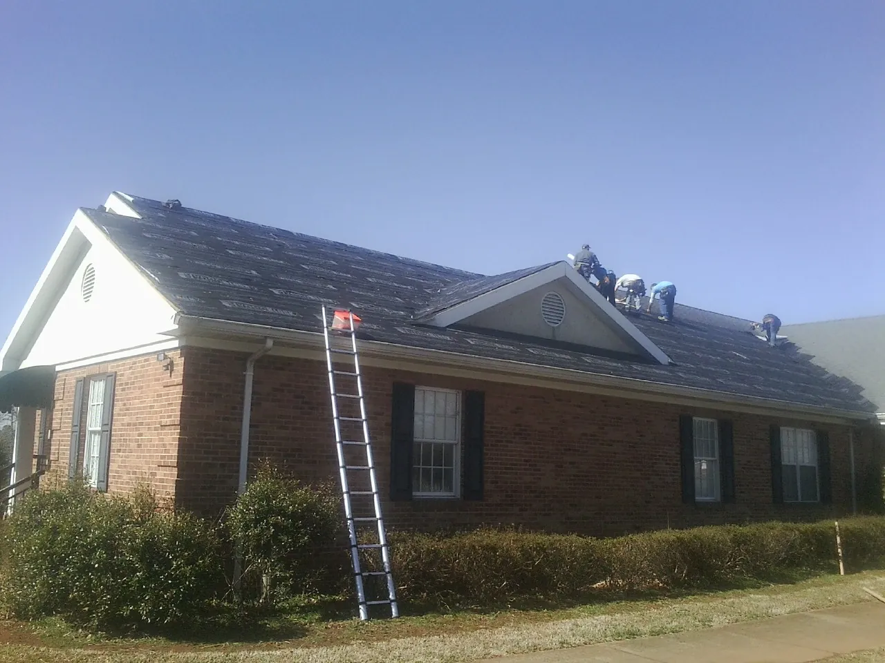 Crew tearing shingles off a brick ranch roof with a ladder set — Emergency Roof Repair work by our crew in Sprague