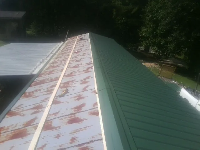 Old rusted panels beside newly installed green metal roofing — Wind Damage Roof Repair by Roofing Brothers in Sprague