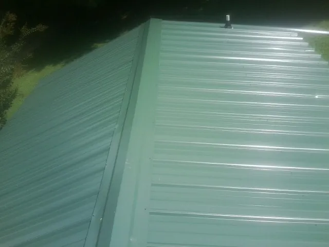 New green metal panels meeting at the ridge of a roof — Flat Roof Repair work by our crew in Sprague